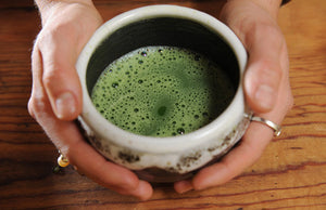 Hands holding ceramic bowl of matcha green tea