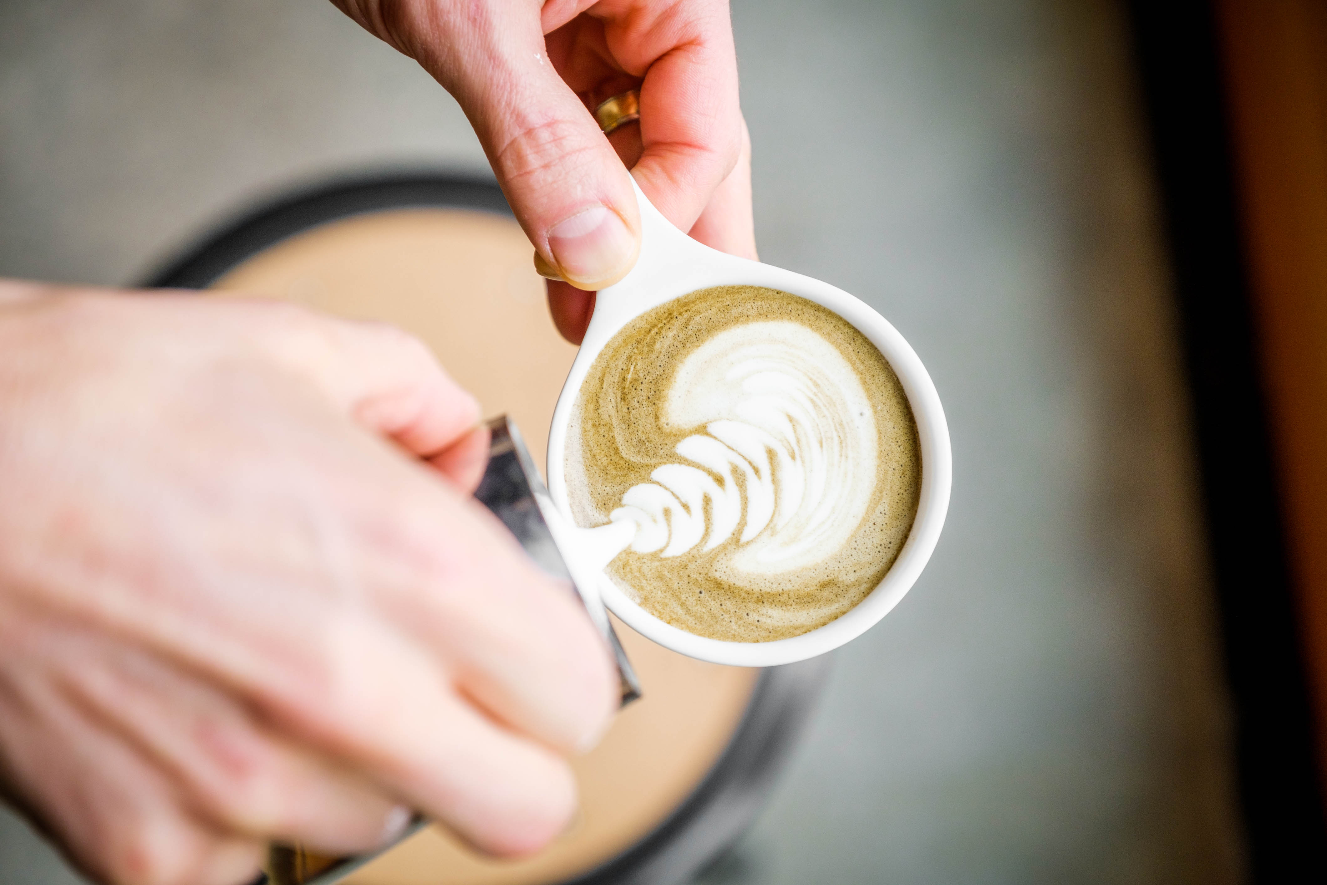 Person making latte art in a cup of Hojicha