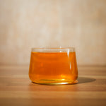 A short, glass tea cup filled with pu-erh tea sits on a wooden table – Mizuba Tea Co.