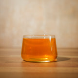 A short, glass tea cup filled with pu-erh tea sits on a wooden table – Mizuba Tea Co.