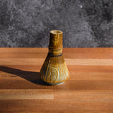 Dark wood matcha whisk resting on a ceramic stand