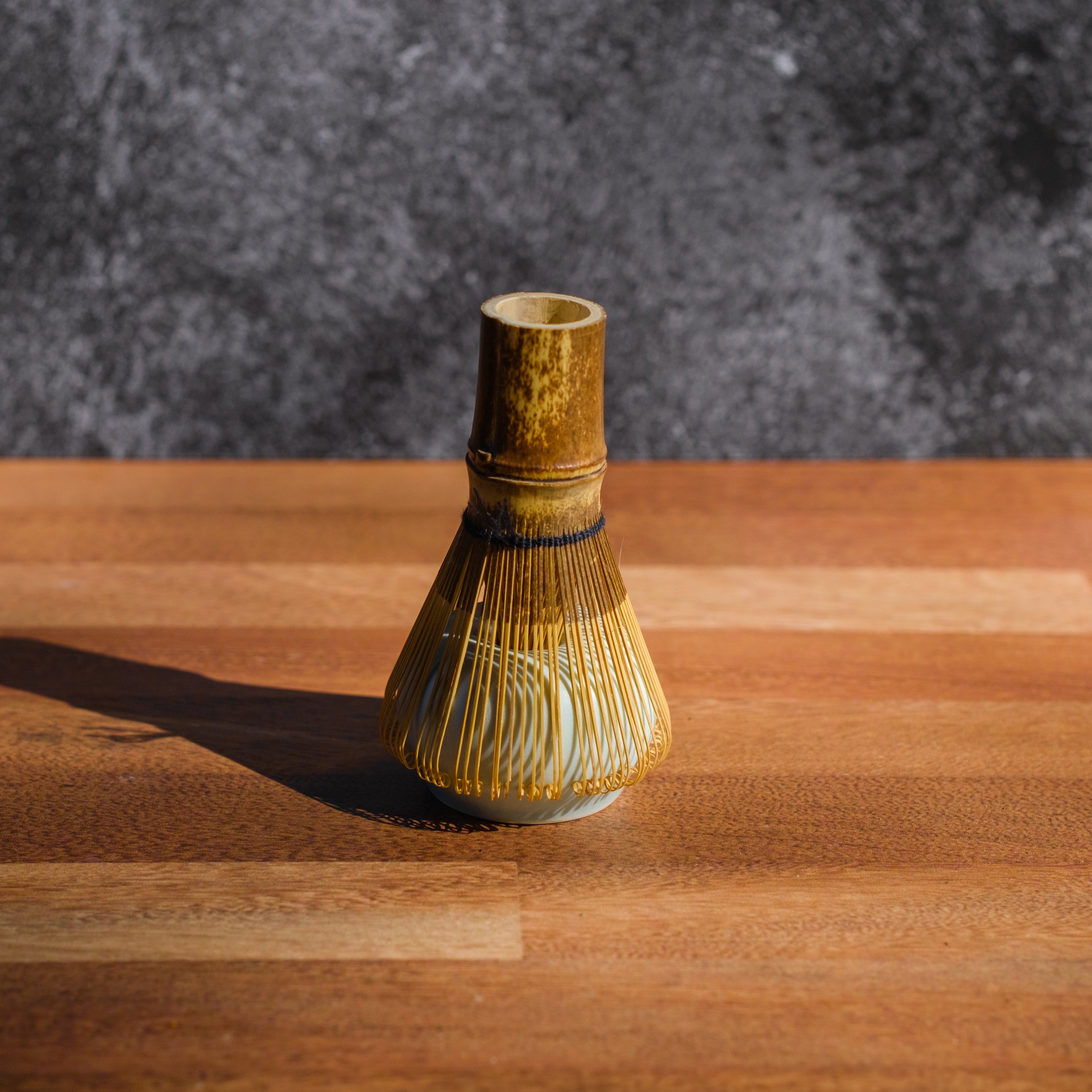 Dark wood matcha whisk resting on a ceramic stand