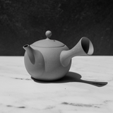 Gray, handmade Tokoname Japanese porcelain teapot on a marble surface with a dark background.
