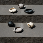 Set of handmade, Japanese Tokoname ceramic teapots and yuzamashi tea tools in beige, black, and grey colors on a stone surface
