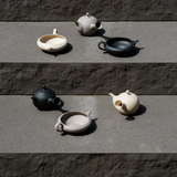 Set of handmade, Japanese Tokoname ceramic teapots and yuzamashi tea tools in beige, black, and grey colors on a stone surface