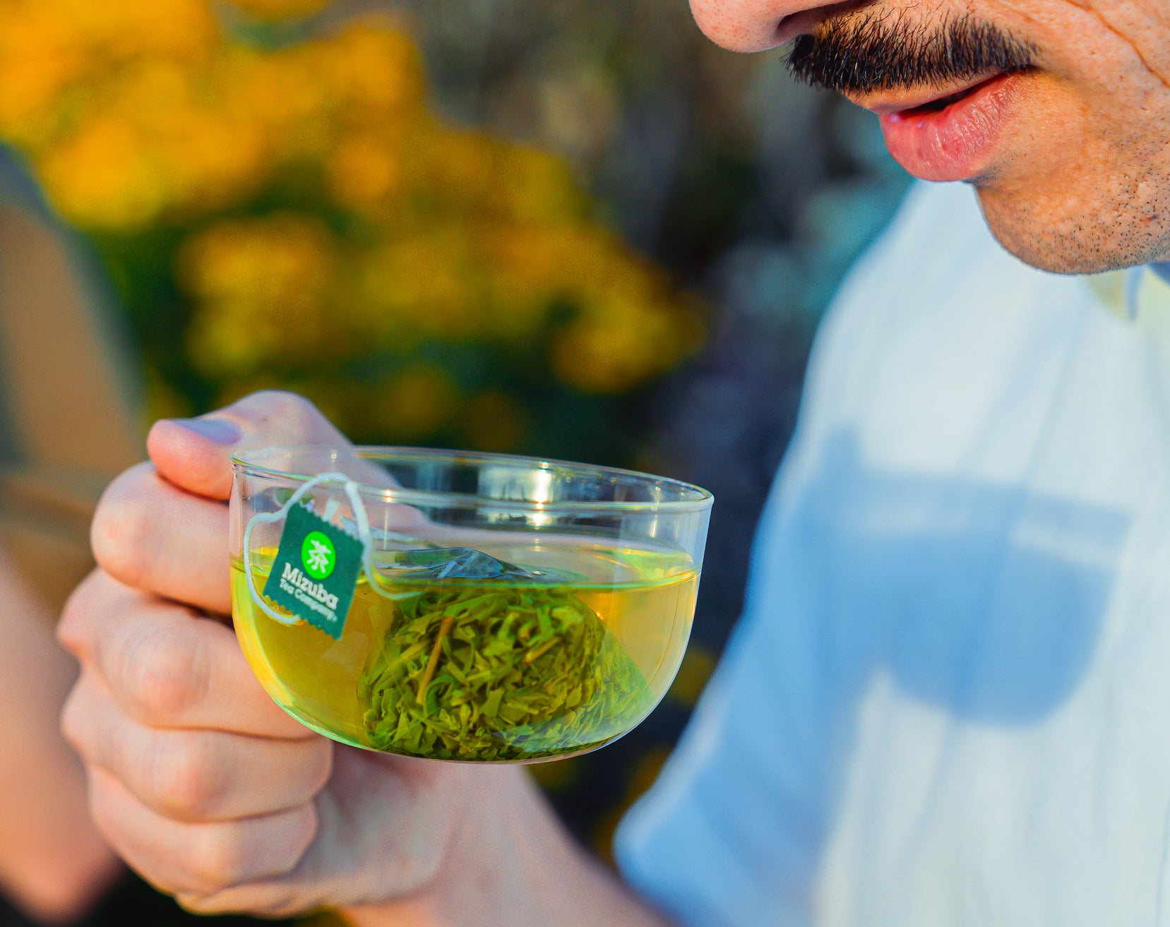 Man with mustache about to sip from a glass cup with a organic green tea sachet inside – Mizuba Tea co.