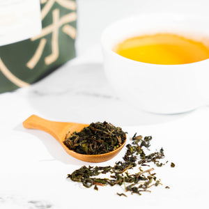 Tea scoop filled with oolong tea leaves and a cup of brewed tea in the background