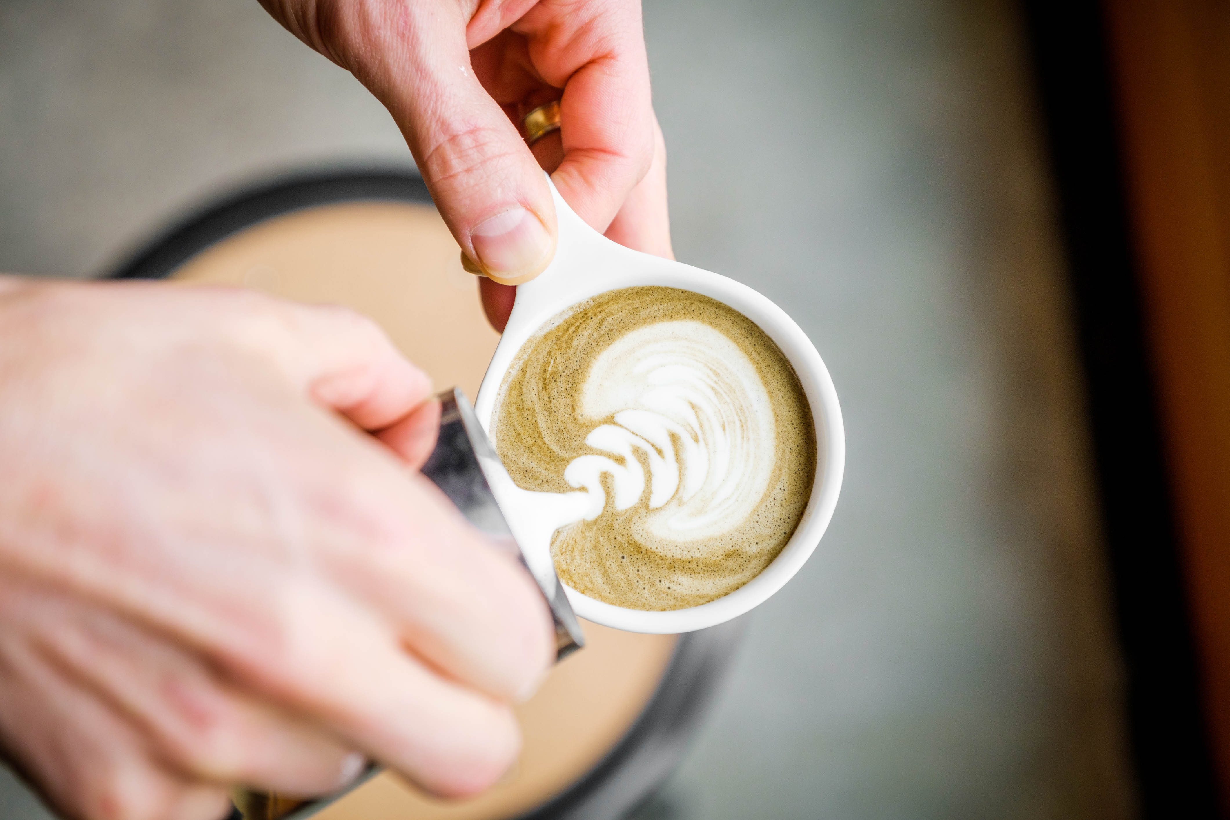 Two hands pouring a hojicha roasted green tea latte in a coffee shop - Mizuba Tea Co.