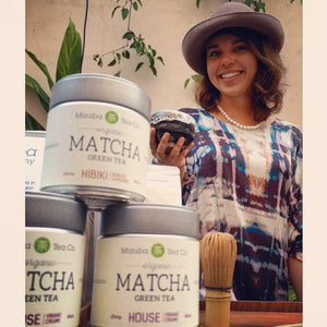 Three matcha tins in front of smiling woman