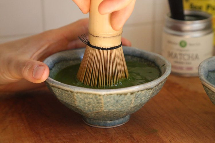 Hand holding a chawan tea bowl while whisking matcha green tea