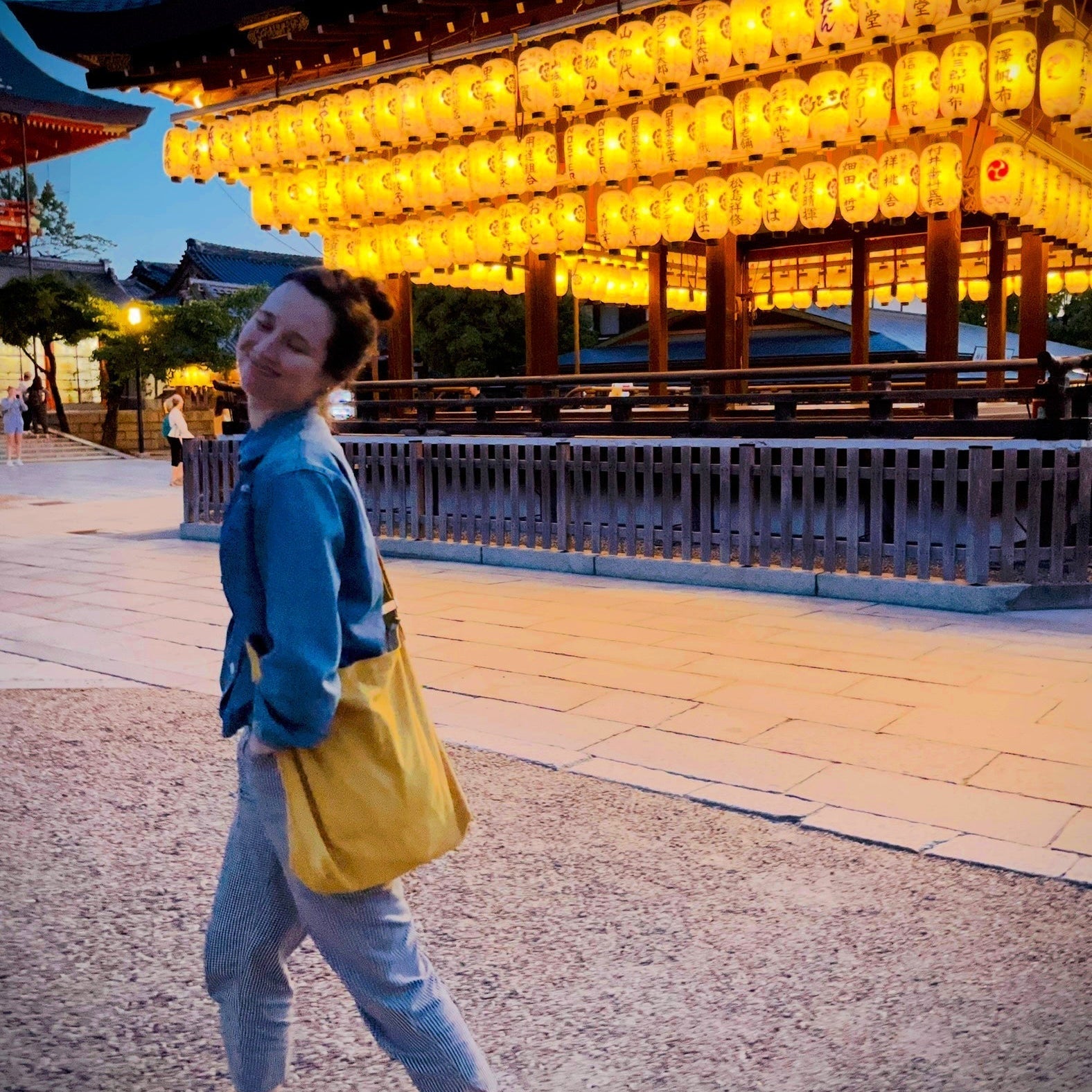 Woman walks happily by a temple adorned with lanterns in Kyoto, Japan