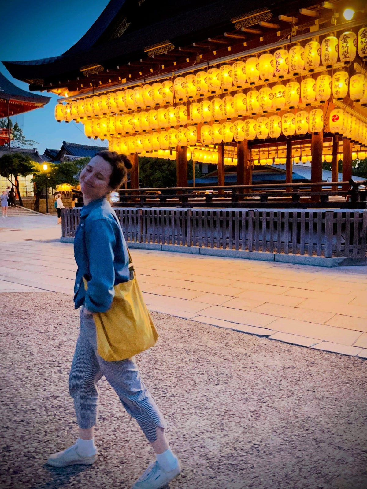 Woman walks happily by a temple adorned with lanterns in Kyoto, Japan