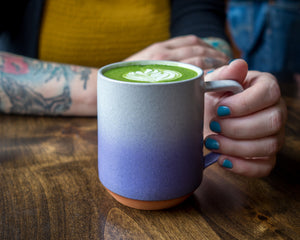 Woman holds matcha latte in purple mug