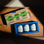 A ceremonial matcha tasting set from Mizuba Tea Co. displayed on a wooden surface in natural sunlight. The three tins read, "Tsuyuhikari, Shirakawa, and Yorokobi Matcha."