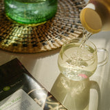 Tea is poured into a glass teacup sitting on a table next to a bag of loose leaf sencha yuzu