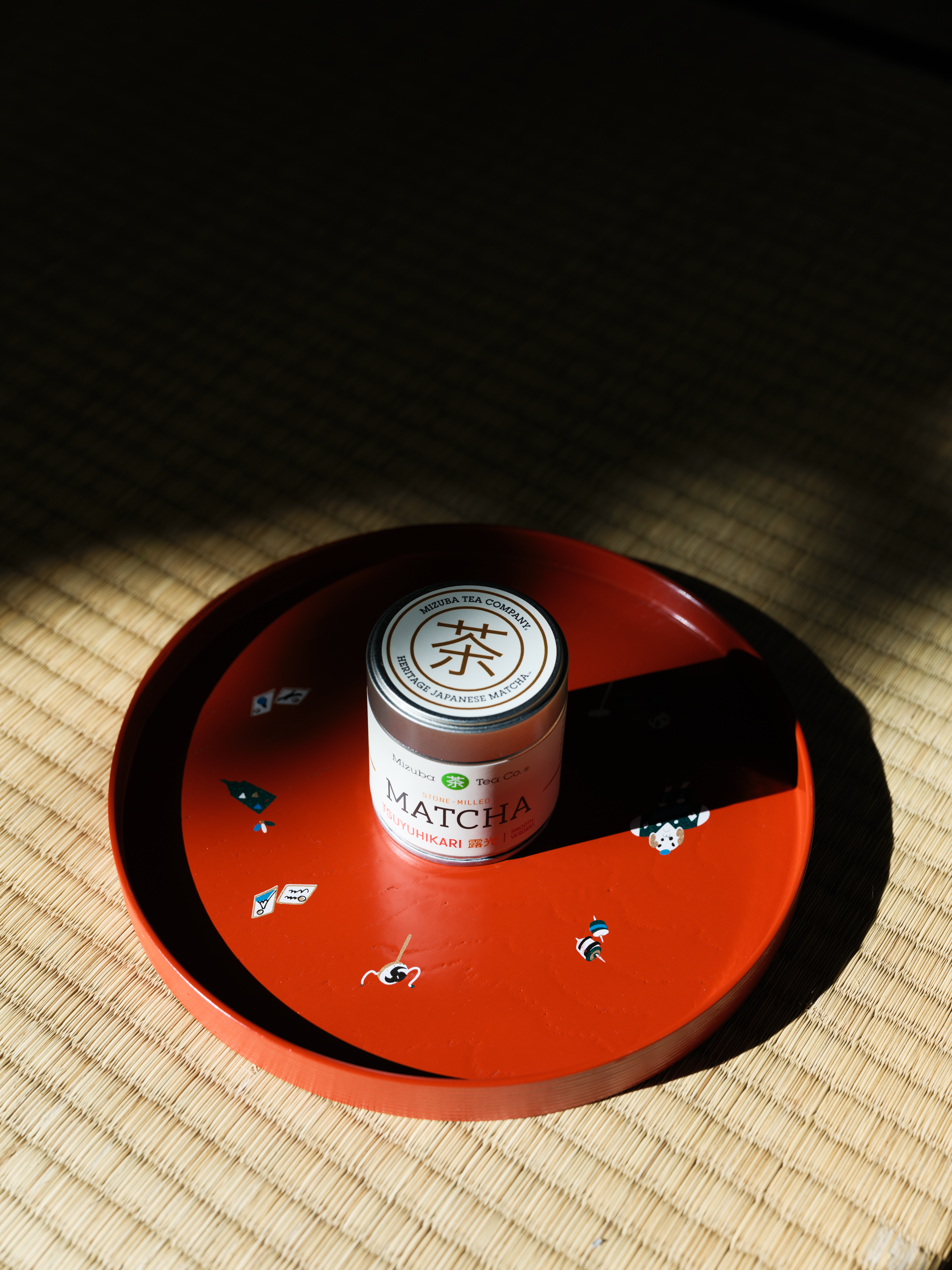 Matcha powder tin container on a red tray placed on tatami mat with a dark background