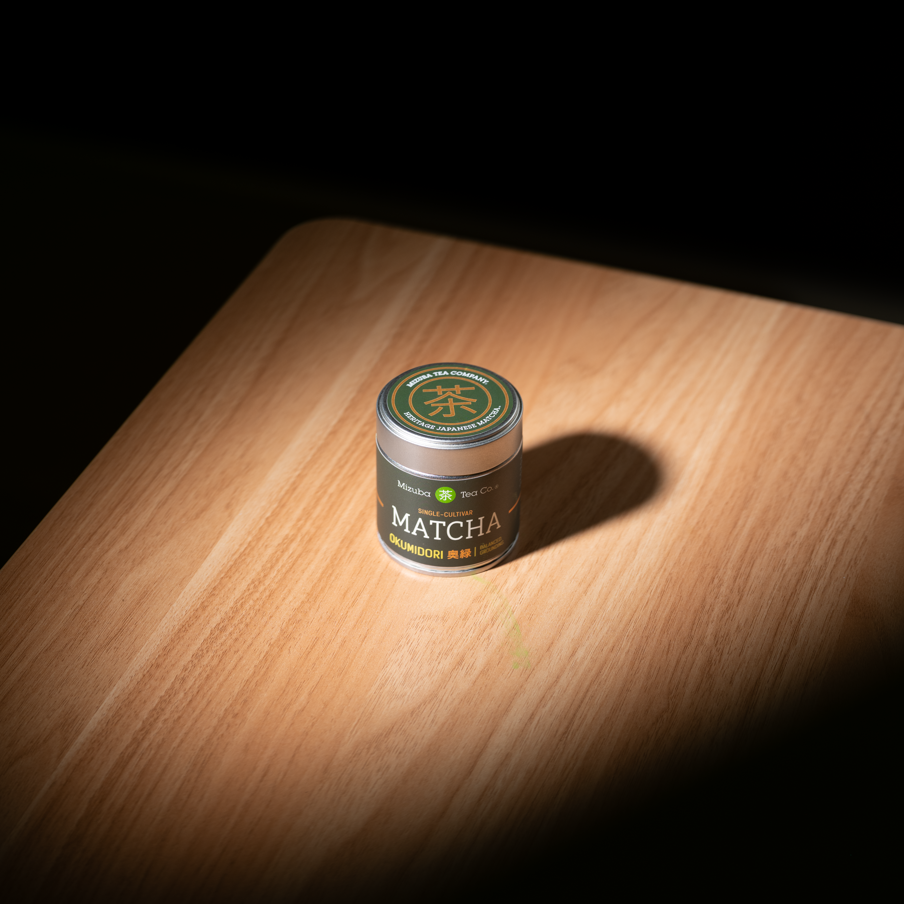 Mizuba Matcha Okumidori green tea container on a wooden surface with a dark background
