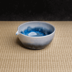 Blue and white gradient ceramic matcha green tea chawan bowl on a tatami woven surface with a dark background