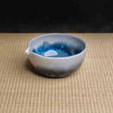 Blue and white gradient ceramic matcha green tea chawan bowl on a tatami woven surface with a dark background