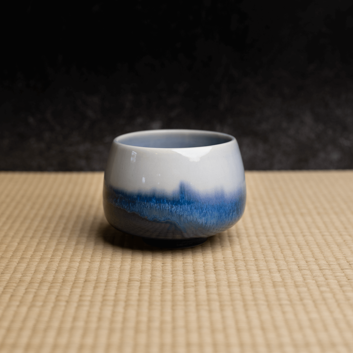 Handmade ceramic cup by OWIU with blue gradient on a tatami mat.