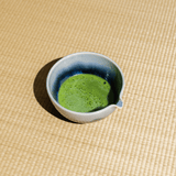 Ceramic cup with frothed matcha green tea on a woven tatami surface