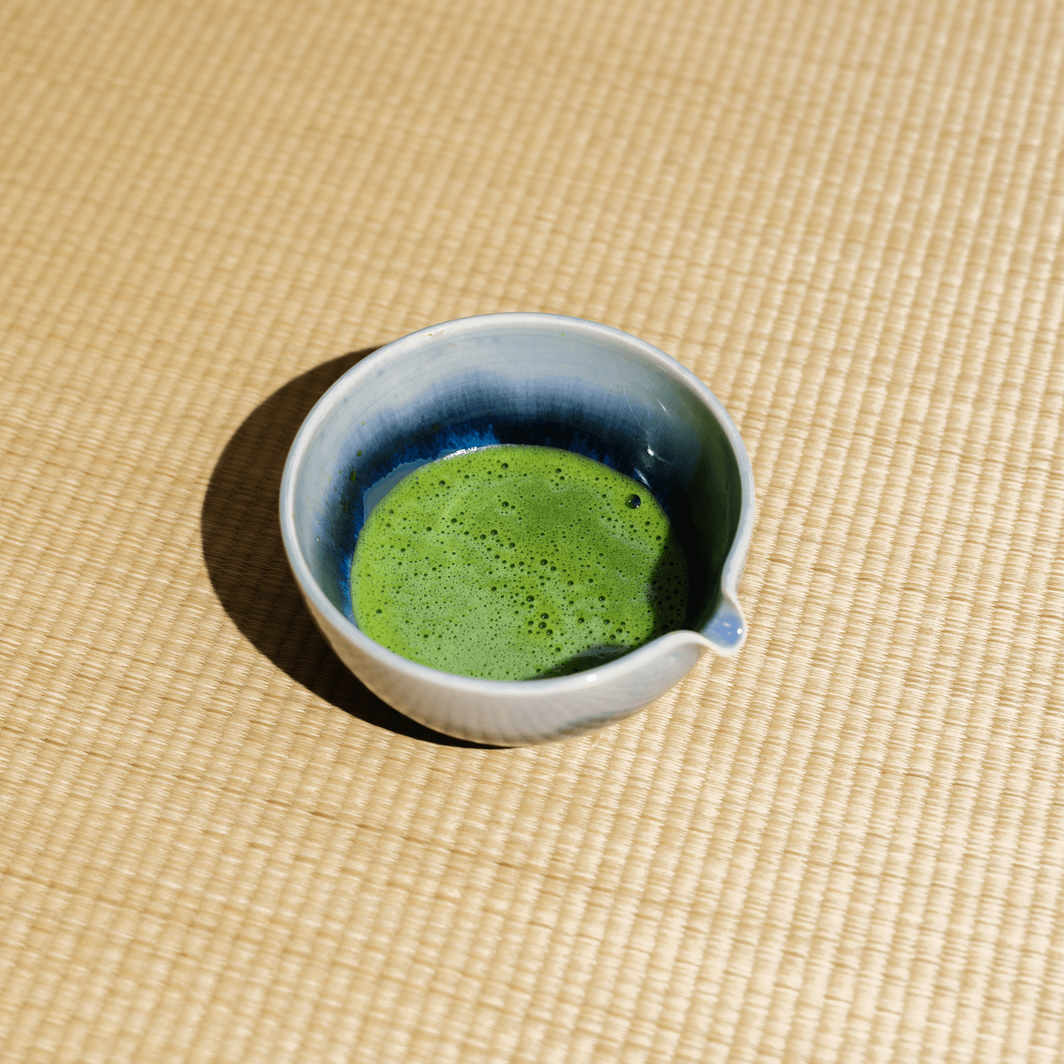 Ceramic cup with frothed matcha green tea on a woven tatami surface