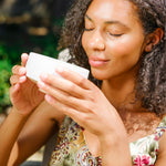 Woman with eyes closed smiles as she is about to sip matcha green tea from a white chawan tea bowl