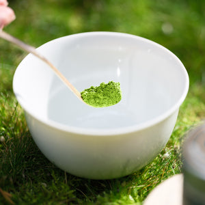 A bamboo scoop showcases fresh, organic matcha green tea over a pure white porcelain chawan tea bowl