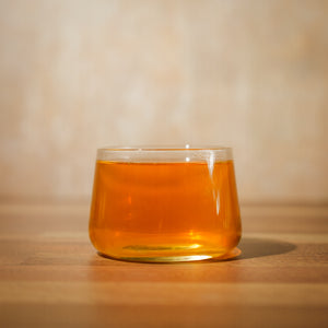 A short, glass tea cup filled with pu-erh tea sits on a wooden table.