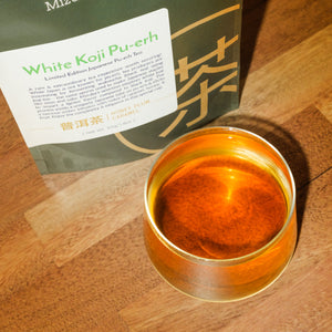 An overhead view showcases amber pu-erh tea in a glass tea cup. The tea's packaging is in the background.