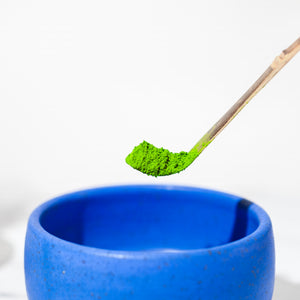 A close-up shot of bright green powdered matcha green tea over a cerulean blue matcha bowl