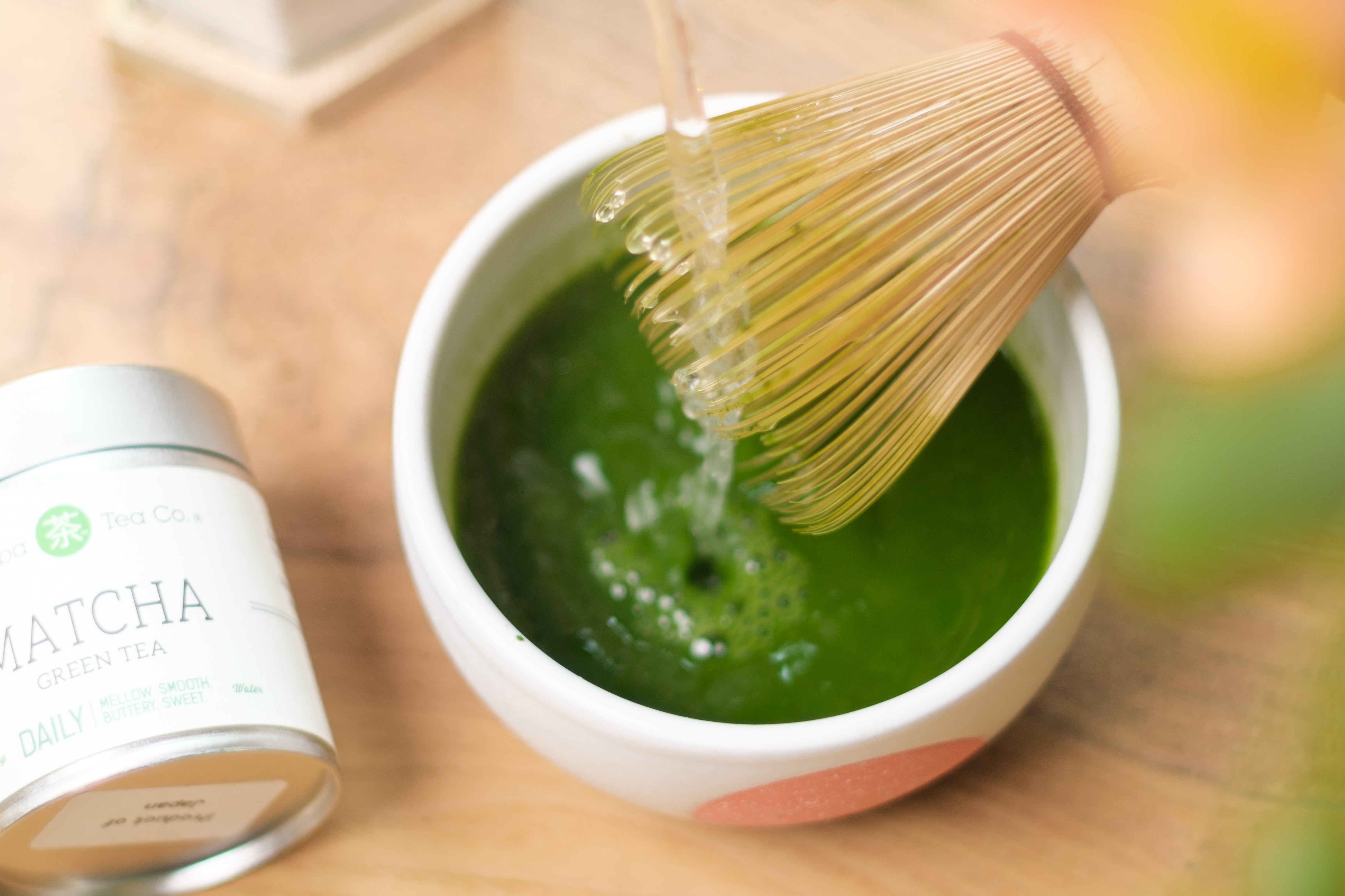 Water poured into a bowl  of matcha with a whisk next to a tin of Mizuba Daily Matcha