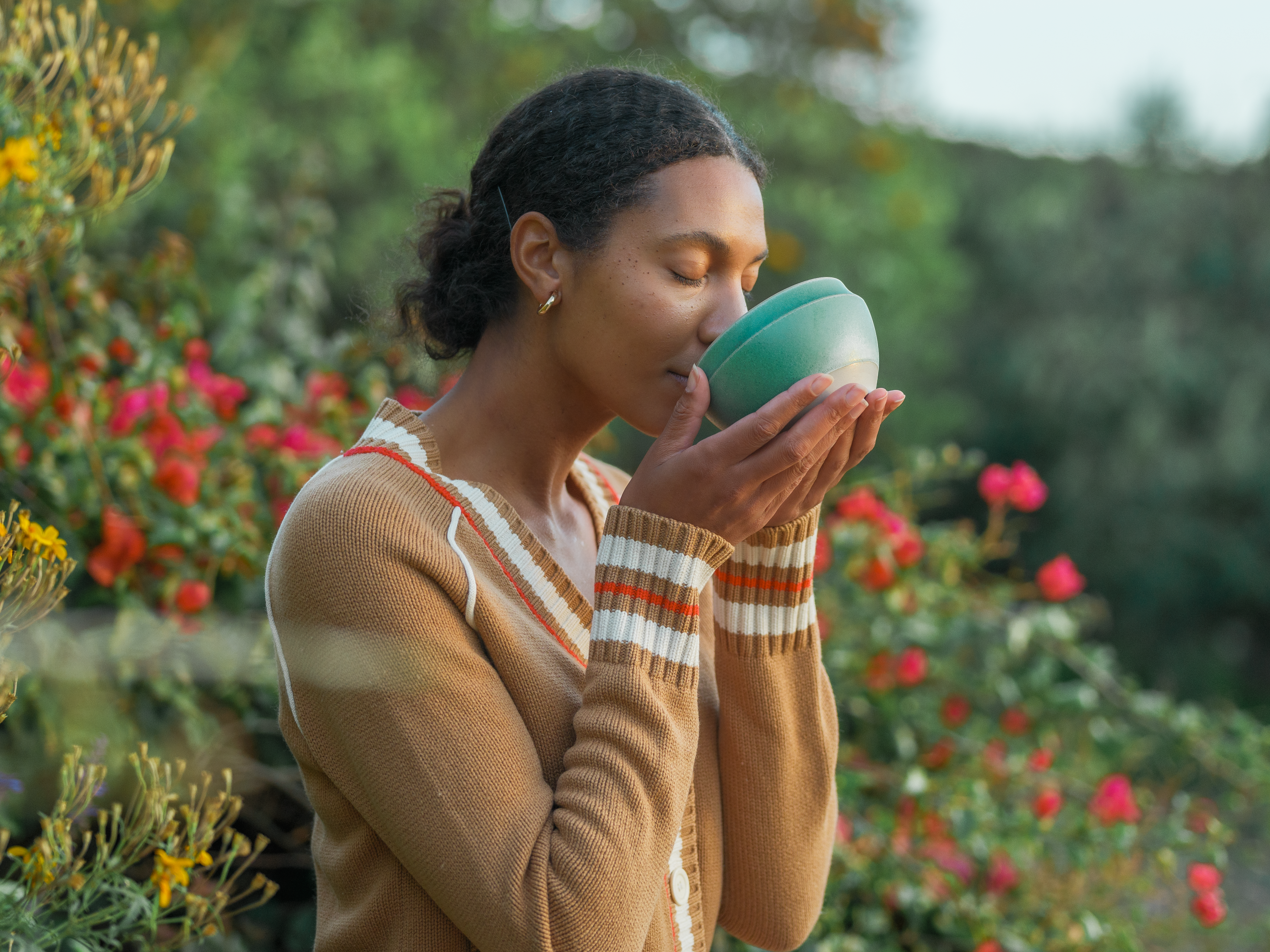 Woman sips Mizuba matcha from green chawan tea bowl in a garden.