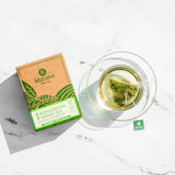 Box of Mizuba Tea Company plant based tea sachets lays next to a brewing tea bag in a glass cup.