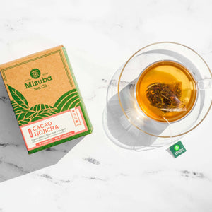 Mizuba Tea Co. 15 count cacao hojicha tea bag. The box is featured next to a brewing sachet in a glass tea cup.