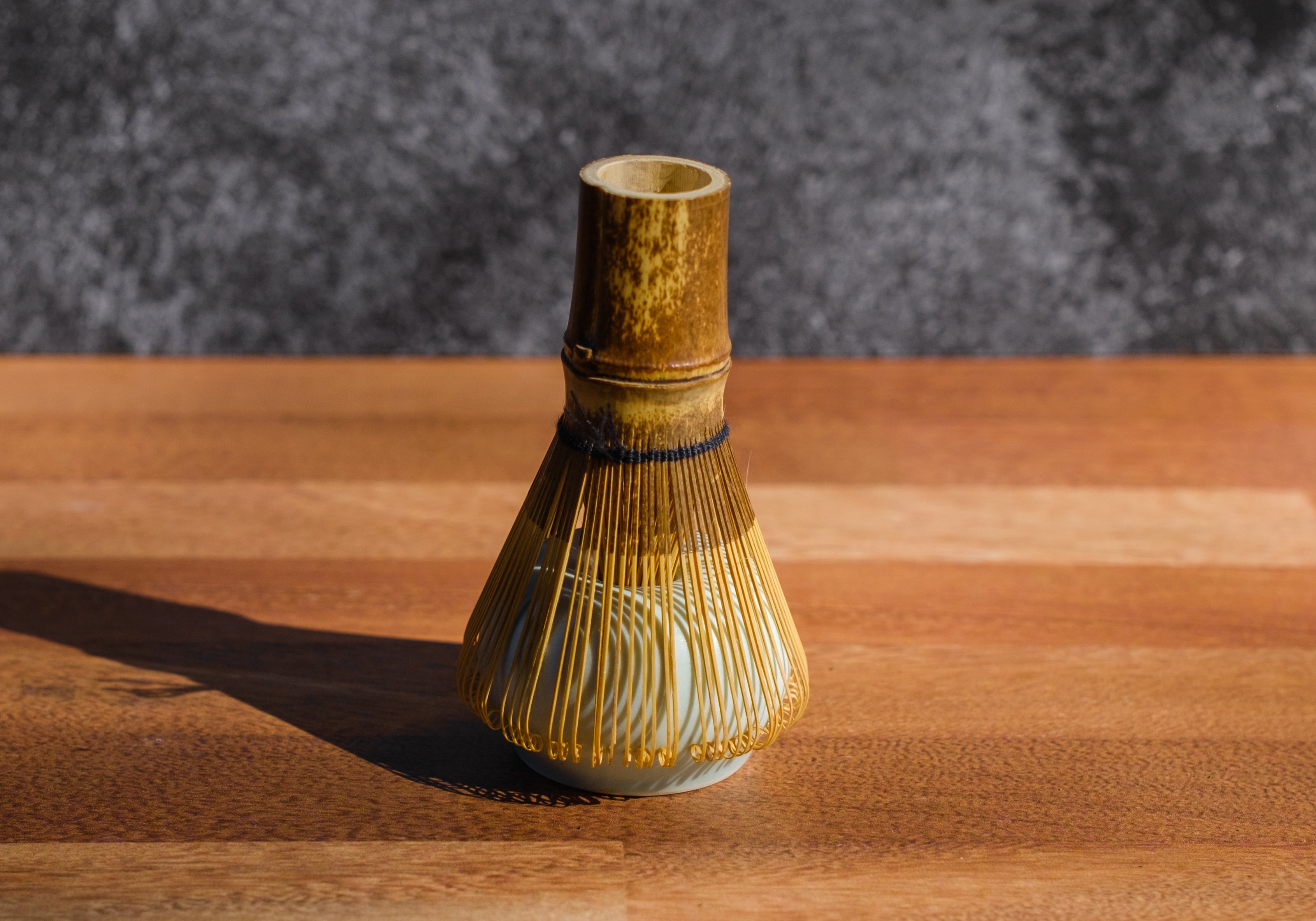 Dark wood matcha whisk resting on a ceramic stand