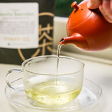 A brew of sencha saemidori by Mizuba Tea Company poured from a red Tokoname Kyusu into a glass tea cup.