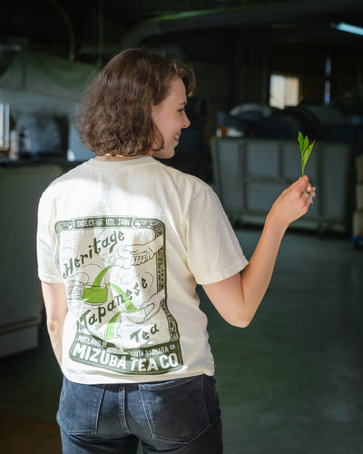 Woman wearing a custom illustrated shirt with Japanese tea design holds a fresh tea leaf from the fields of Japan