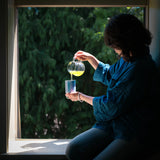 A woman pours freshly brewed shincha Japanese green tea into a blue ceramic cup. 