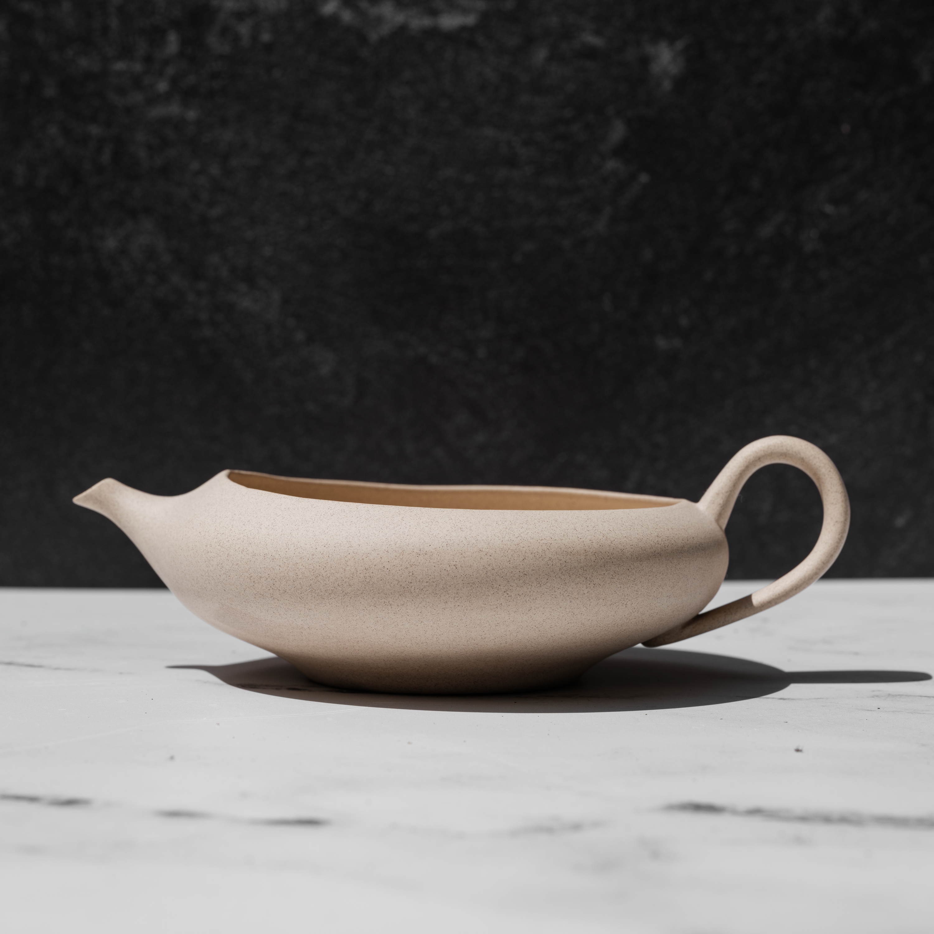 Beige ceramic yuzamashi teapot on a marble surface with a dark background