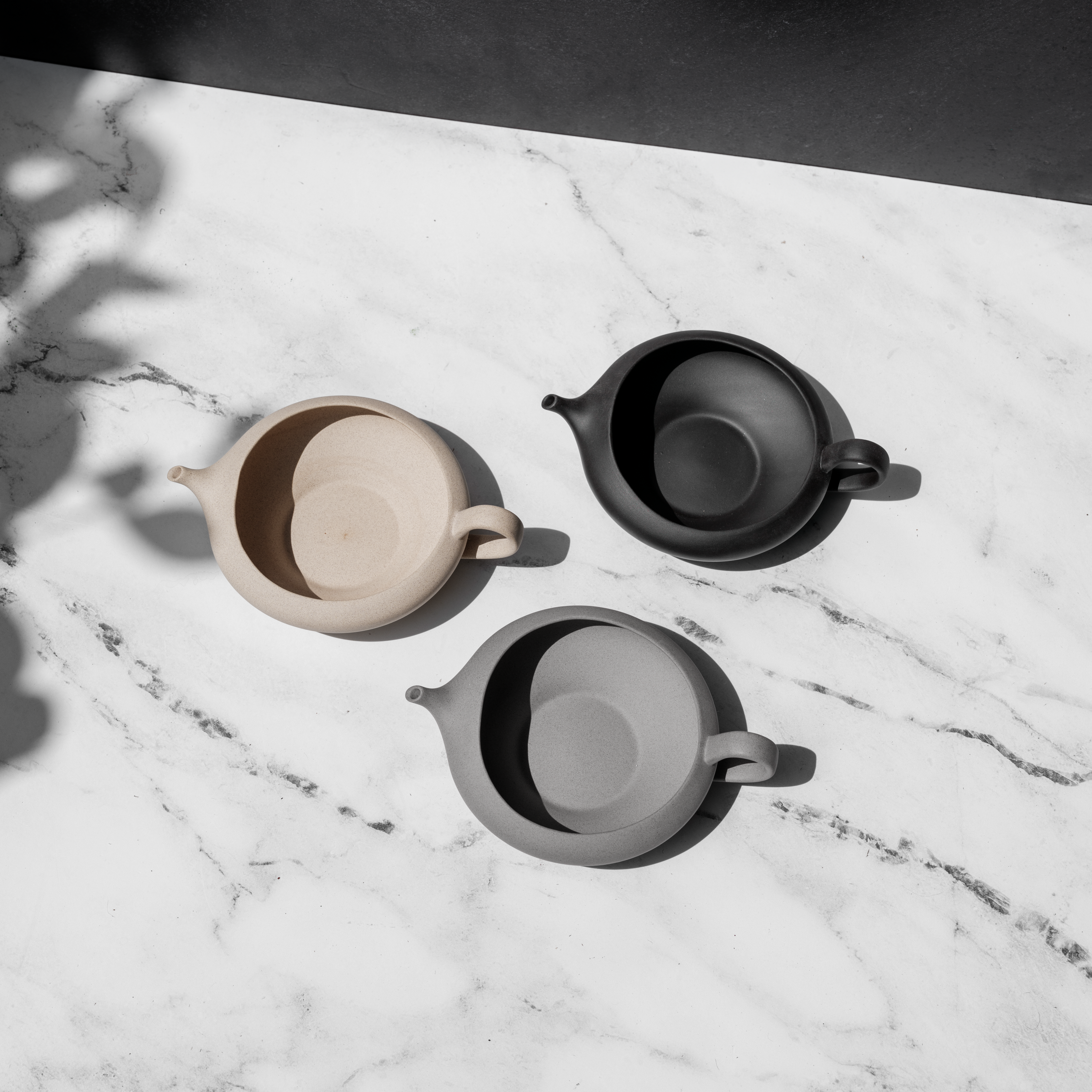 Three ceramic pots in beige, black, and gray on a marble surface
