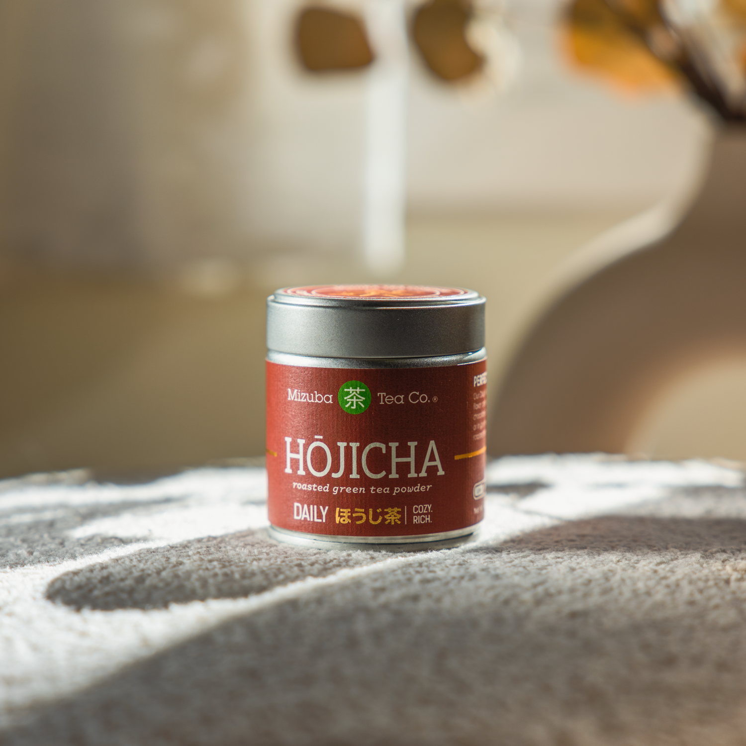 Mizuba Tea Co. Hojicha roasted green tea powder canister on a textured surface with a blurred background