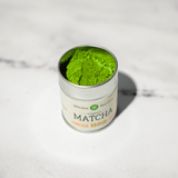 Canister of Mizuba matcha green tea powder on a white marble surface