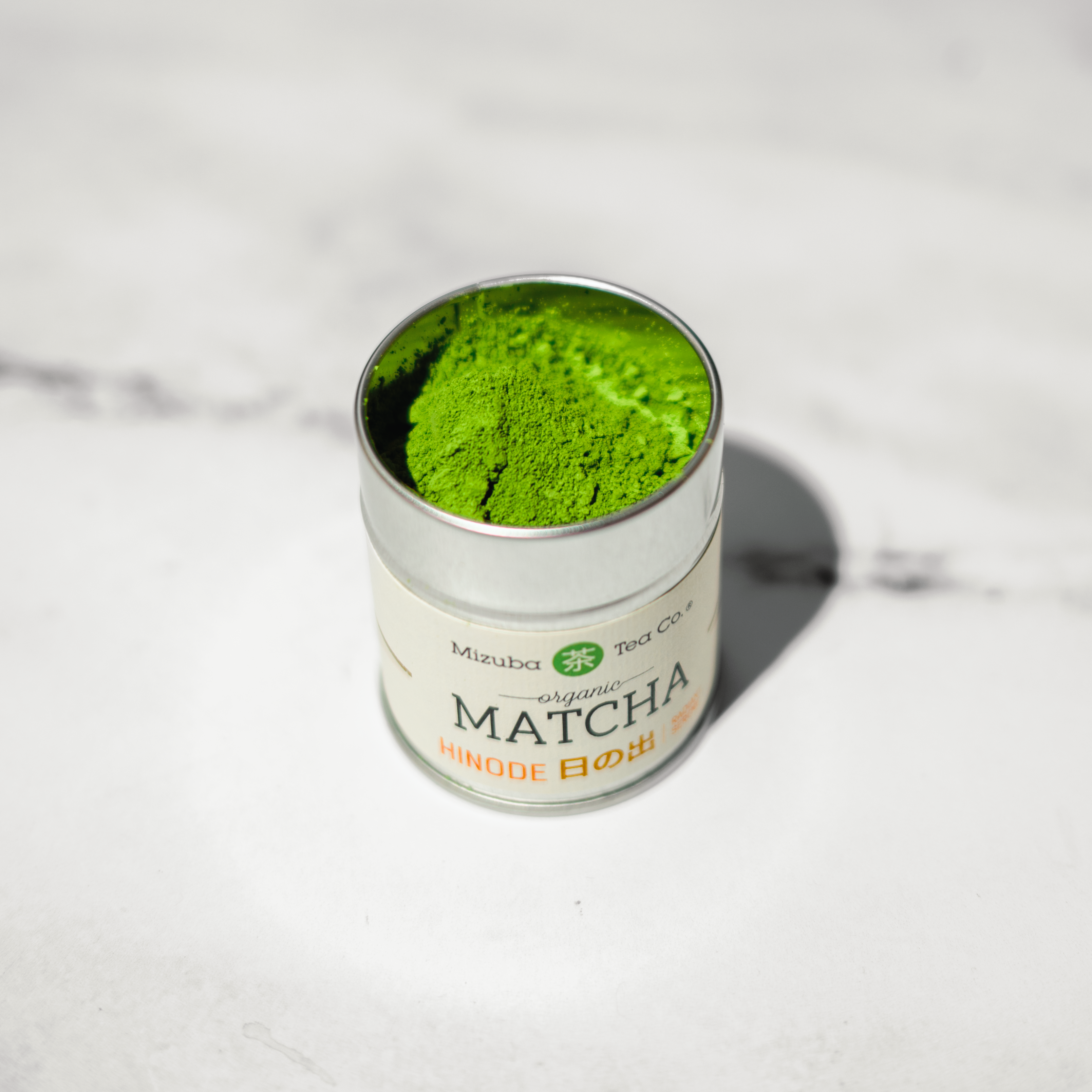 Canister of Mizuba matcha green tea powder on a white marble surface