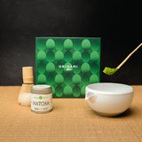 Origami Mizuba Matcha tea set with a chawan ceramic bowl, Yama matcha tin, chasen whisk stand, genuine chashaku scoop, and packaging on a wooden surface.