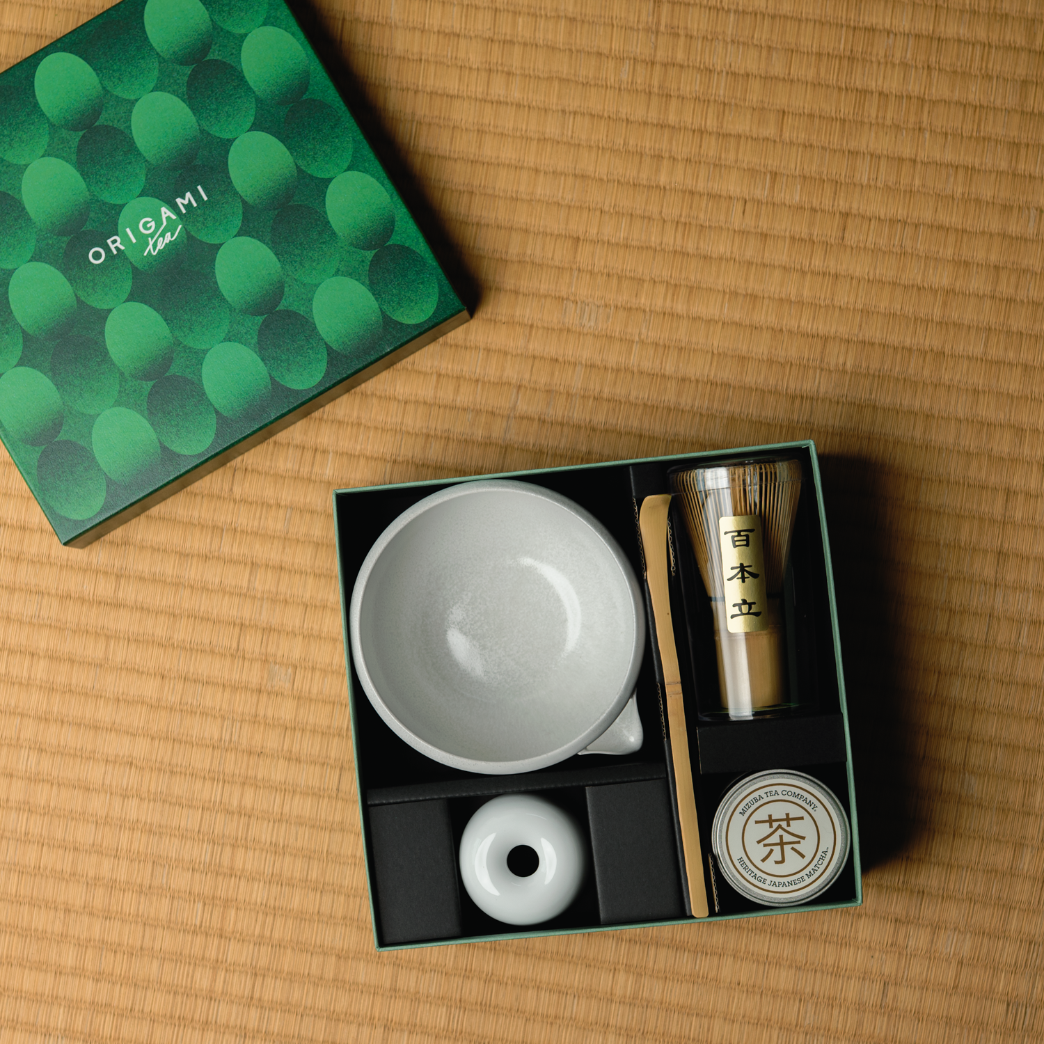 Tea set with a green box labeled 'Origami Tea' on a tatami mat woven surface.
