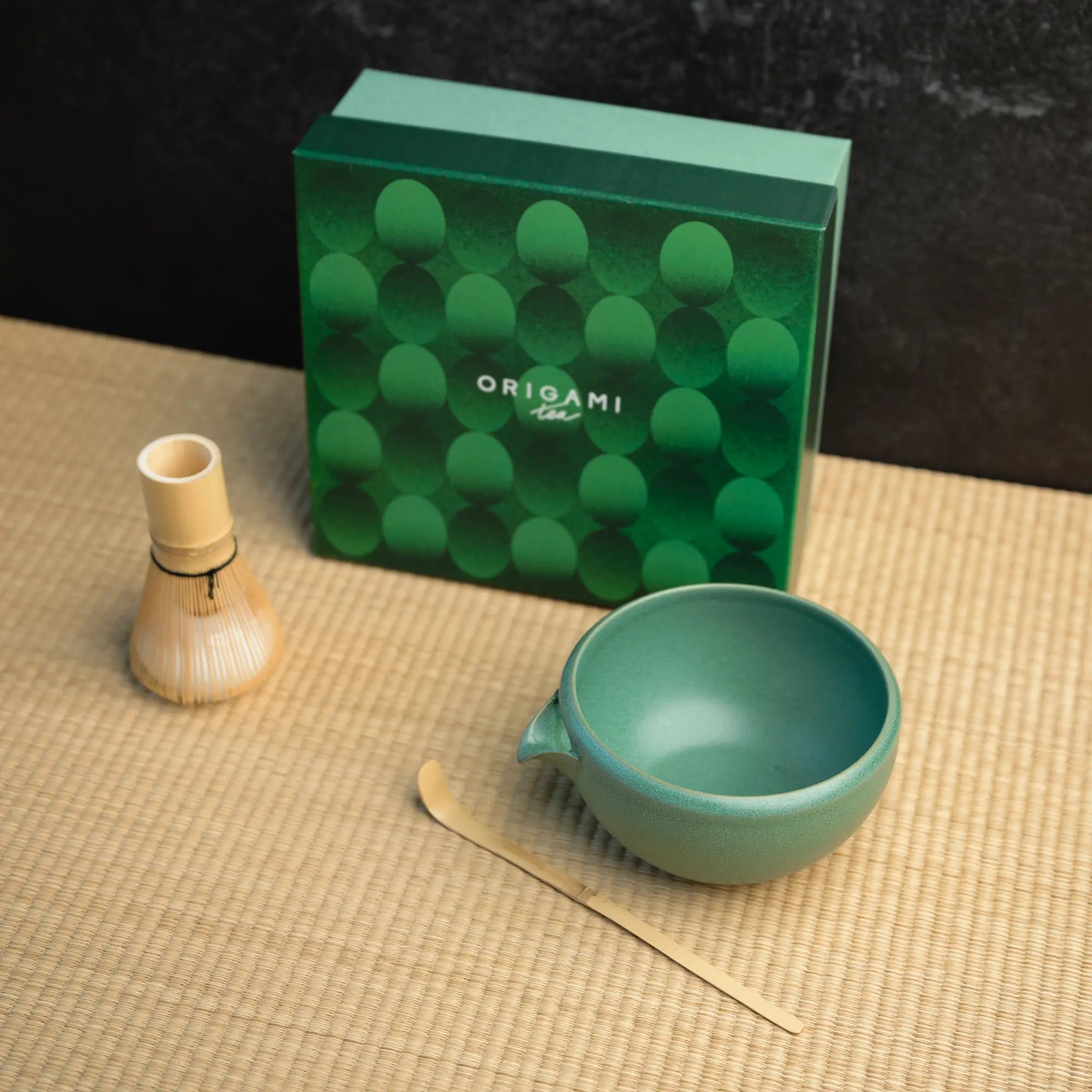 A chasen, chawan, and matcha bowl in front of a green box labeled "Origami Tea"