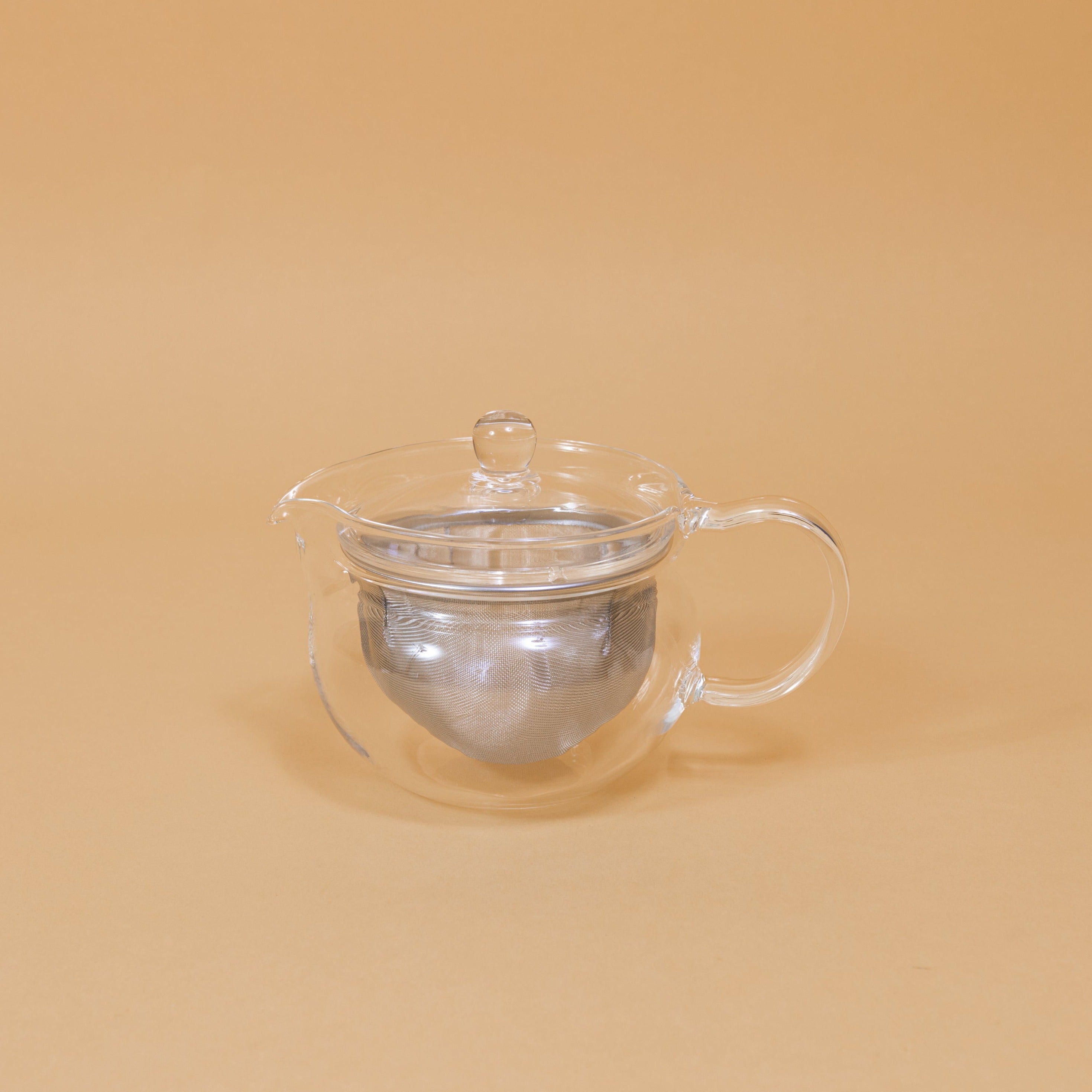 A modern glass teapot sits on a yellow background.