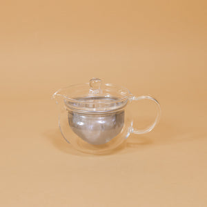 A modern glass teapot sits on a yellow background.