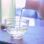 Iced tea is poured from a Hario cold brew bottle into a glass tea cup 